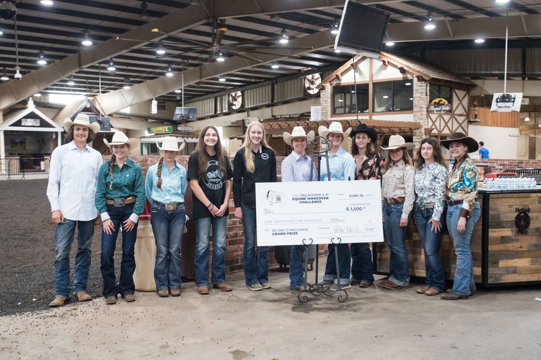 The 2021 Oklahoma 4-H Equine Makeover Contestants at the Finale (11 youth gather around a scholarship winner check in front of an arena)